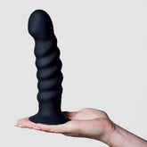 A hand holding the Maia 'Kendall' 8" Silicone Dildo - Black, celebrated for its g-spot stimulation, against a plain background.